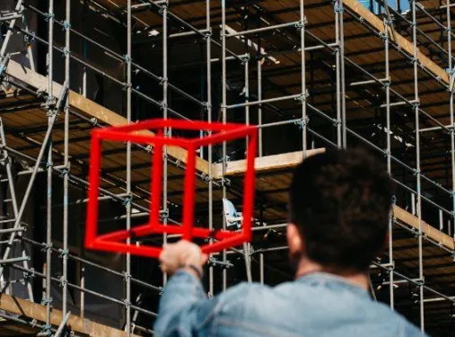 Sfeerbeeld Quion. Man op de rug gefotografeerd terwijl hij een kubus in de lucht houdt voor een gebouw in aanbouw.