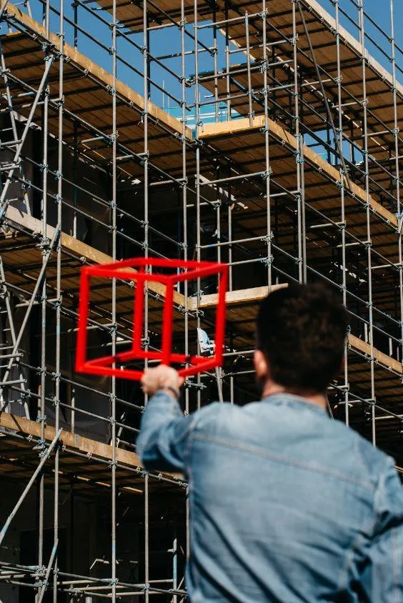 Sfeerbeeld Quion. Man op de rug gefotografeerd terwijl hij een kubus in de lucht houdt voor een gebouw in aanbouw.